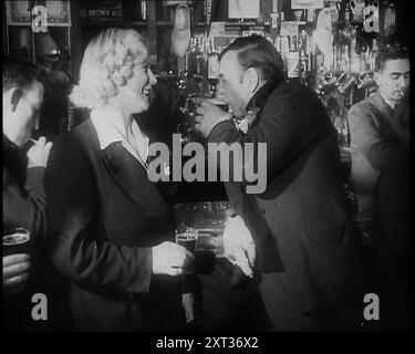 Une femme britannique et un homme britannique debout au Bar tenant des boissons dans une maison publique avec d'autres clients avec le barman derrière eux, 1939. De "Time to Remember - The Reluctant Warriors", 1939 ( Reel 2) ; documentaire sur les événements de 1939 - les préparatifs pour la guerre et les hostilités éclatent. Banque D'Images