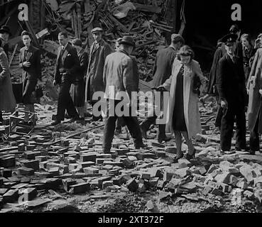 Des foules passant devant des bâtiments bombardés, 1940. La Grande-Bretagne pendant la seconde Guerre mondiale : le Blitz. 'Toute nuit, toute heure, été 1940. Feu et flamme, mort et destruction... n'importe quel matin après à Londres - ou est-ce Coventry, Bristol, Portsmouth? Liverpool, Belfast, Birmingham ? Plymouth ou Glasgow?...pourtant, avec chaque aube, merveilleux comment l'habitude survit. Il est difficile de tuer la vie normale d'une grande ville, difficile de tuer l'habitude de se mettre au travail le matin. Mais quelle méconnaissance à trouver sur votre voyage trop familier. Trous où il n'y avait pas de trous hier, pas de maisons où hier' Banque D'Images