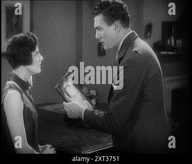 Carl Brisson et Lilian Hall-Davis agissant dans une scène. Carl Brisson tient une photo encadrée d'un autre homme, des années 1920 "Pourquoi Carl Brisson, survolant un drame passionné avec Lilian Hall-Davis". De "Time to Remember - came the Dawn", 1925 (bobine 1) ; aperçu de l'industrie cinématographique britannique des années 1920 - extraits de grands films muets et de nouvelles. Banque D'Images