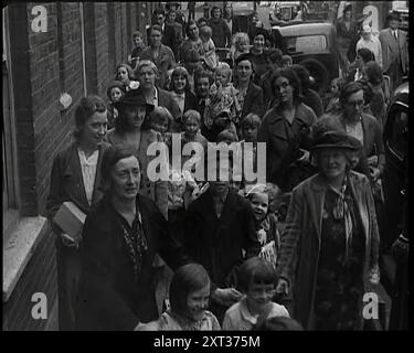 Femmes et enfants britanniques évacués marchant le long du trottoir d'une rue résidentielle à côté d'une ligne de maisons mitoyennes avec des voitures garées dans la route et d'autres adultes marchant à proximité, 1939. De "Time to Remember - The Reluctant Warriors", 1939 (bobine 1) ; documentaire sur les événements de 1939 - les préparatifs de la guerre et les hostilités éclatent. Banque D'Images