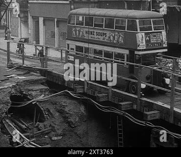 Un bus traversant un pont en bois, Londres, 1940. La Grande-Bretagne pendant la seconde Guerre mondiale : le Blitz. Le bus numéro 14 continue de circuler sur son itinéraire en utilisant un pont temporaire sur les dégâts causés par les bombes. 'Toute nuit, toute heure, été 1940. Feu et flamme, mort et destruction... n'importe quel matin après à Londres... mais avec chaque aube de ravages frais, merveilleux comment l'habitude survit. Il est difficile de tuer la vie normale d'une grande ville, difficile de tuer l'habitude de se mettre au travail le matin. Mais quelle méconnaissance à trouver sur votre voyage trop familier. Trous où il n'y avait pas de trous hier, pas de maisons où hier' Banque D'Images