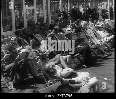 Lignes d'hommes et de femmes assis dans des transats sur un quai à Brighton avec plusieurs journaux de lecture, 1939. De "Time to Remember - The Reluctant Warriors", 1939 (bobine 1) ; documentaire sur les événements de 1939 - les préparatifs de la guerre et les hostilités éclatent. Banque D'Images