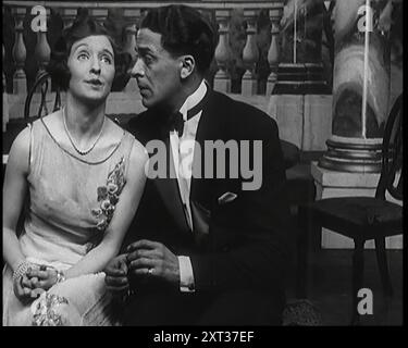 Jack Buchanan et June Knight assis sur un banc ensemble. Buchanan regardant mal à l'aise alors que June est assis de plus en plus près de lui, dans les années 1920 «...une magie comme les humeurs dansantes de Jack Buchanan et June. Un sens a-t-il déjà été si débordant ? Assez désarmant ? Comme leur effort semblait sans effort ». De "Time to Remember - on Stage in the Twenties", 1927 (bobine 3) ; un regard sur les coulisses du théâtre dans les années 1920 Banque D'Images