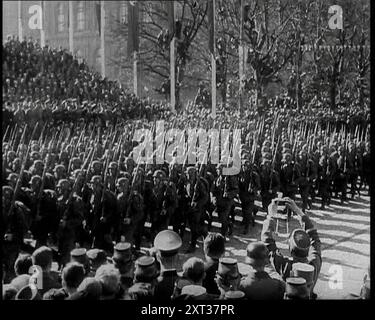 Une formation de soldats allemands masculins marchant devant une plate-forme de fonctionnaires sur une rue viennoise bordée d'arbres avec d'autres soldats et civils regardant avec un soldat tenant un appareil photo dans les airs et photographiant l'occasion, 1938. De "Time to Remember - Wind Up week", 1938 (bobine 1) ; film documentaire sur 1938 - les gens prennent conscience de la menace croissante de la guerre. Banque D'Images