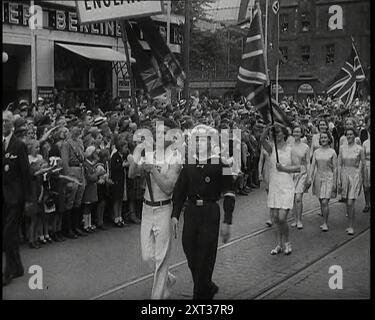 The English contingent in the Parade of the World Congress for Leisure Time and Recreation 1936 Walking along a Hamburg Street passant un bar dirigé par un homme en pantalons et une veste avec un homme en robe navale avec des femmes en robes courtes derrière Waving Union Flags, 1938. De "Time to Remember - Wind Up week", 1938 (bobine 1) ; film documentaire sur 1938 - les gens prennent conscience de la menace croissante de la guerre. Banque D'Images