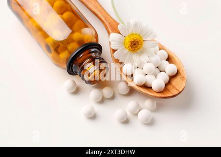 Remède homéopathique. Cuillère avec des pilules, bouteille et fleur de camomille sur fond blanc Banque D'Images