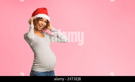 Femme enceinte excité à Santa hat posing sur fond gris Banque D'Images