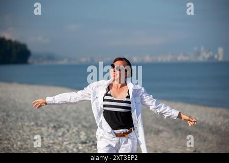 Une femme portant une chemise blanche marche le long du bord de mer. Banque D'Images