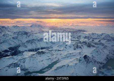 Une photographie aérienne à couper le souffle capturant les sommets enneigés des Alpes suisses baignés dans la lueur chaude d'un coucher de soleil Banque D'Images