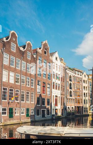 Un soleil éclatant illumine les maisons de canal classiques d'Amsterdam avec des façades à pignons distinctes le long d'une voie d'eau calme, capturant l'essence de l'architecture néerlandaise Banque D'Images