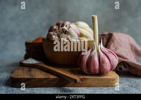 Bulbes d'ail frais et gousses individuelles affichés sur une planche à découper en bois, accompagnés d'un bol en bois, faisant un thème de cuisine visuellement riche Banque D'Images