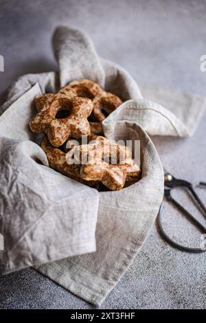 Vue de dessus de biscuits en forme d'étoile en pain d'épice faits maison enveloppés dans un tissu gris, créant une ambiance confortable et rustique. Une paire de ciseaux ajoute une touche Banque D'Images