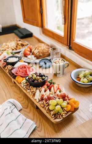 Vue de dessus d'une planche de charcuterie élaborée remplie d'une variété de viandes, fromages, noix et fruits frais, servis sur une table en bois rustique à côté d'un b. Banque D'Images
