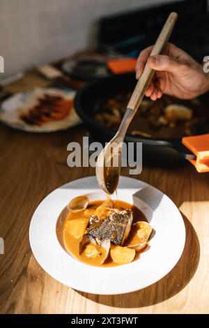 Plan recadré méconnaissable d'une main de chef versant une riche sauce ragoût sur un plat de fruits de mer magnifiquement plaqué avec un poisson doré, croustillant et doux Banque D'Images