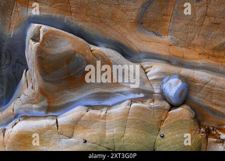 Vue détaillée d'une falaise côtière mettant en valeur l'art naturel exquis dans les couches d'ardoise et les quartzites, avec une palette de couleurs mélangeant l'orange subtil Banque D'Images