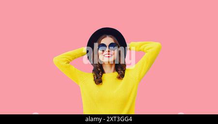 Portrait de jeune femme heureuse élégante portant un chapeau rond noir, pull jaune sur fond rose Banque D'Images