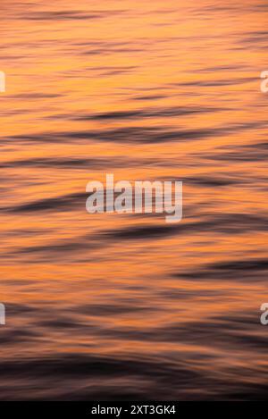 Cette image capture la beauté sereine de l'océan au coucher du soleil, avec de douces ondulations baignées de teintes dorées qui créent une atmosphère calme et tranquille Banque D'Images