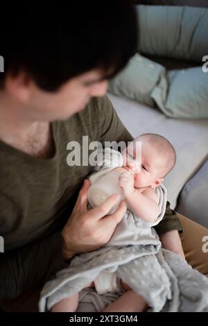 Une image réconfortante capturant un jeune père tenant et nourrissant son nouveau-né avec un biberon à la maison, montrant un lien étroit et nourrissant Banque D'Images