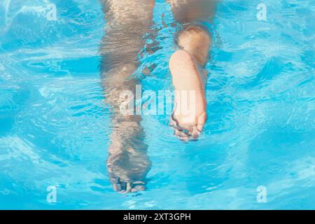 Vue rapprochée de deux pieds flottant doucement sur l'eau bleue claire de la piscine, capturant un moment de calme et de sérénité lors d'une baignade tranquille Banque D'Images