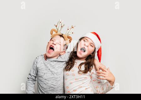 Deux enfants joyeux portant des chapeaux de Noël festifs chantant fort et célébrant, avec des expressions de bonheur pur et de joie de Noël Banque D'Images