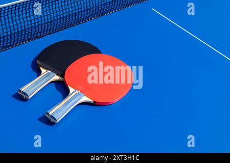 Une image lumineuse capturant deux raquettes de tennis de table, une rouge et une noire, sur une surface de jeu bleu vif avec une partie du filet visible Banque D'Images