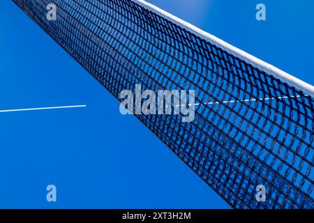 Une vue détaillée se concentrant sur la maille texturée d'un filet de tennis de table, contrastée avec un ciel bleu vif, capturant l'essence d'un set de jeu en plein air Banque D'Images