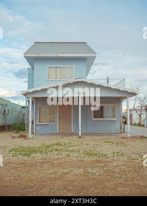 Un bâtiment décrépi de deux étages avec de la peinture écaillée, des fenêtres arborées, et un air général de négligence contre un ciel nuageux. Banque D'Images