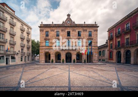 Architecture classique d'un hôtel de ville historique décoré de drapeaux espagnols et européens dans une place vide de Gijon. Banque D'Images