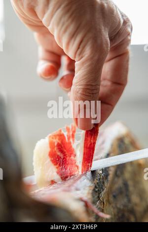 Une image en gros plan d'une main tranchant habilement un mince morceau de jambon ibérique le persillage et la texture de la viande sont mis en valeur, capturant les artisans Banque D'Images