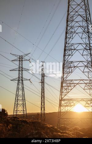 Les tours de transmission d'énergie se dressent face à un coucher de soleil doré dans l'Espagne rurale, mettant en valeur l'infrastructure d'une centrale hydroélectrique. Banque D'Images