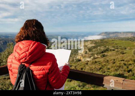 Une femme en veste rouge se tient au point de vue de Las Janas à Salamanque, lisant une carte sur fond de vues montagneuses expansives sous un clair Banque D'Images