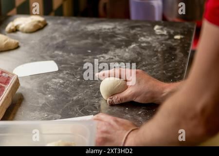 Un cuisinier professionnel façonne la pâte à pizza fraîche sur une surface farinée, en se concentrant sur la création d'une base parfaite pour la pizza Banque D'Images