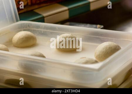 Boules de pâte à pizza crues et parfaitement formées laissées lever dans un plateau en plastique transparent, capturant les étapes initiales de la préparation de la pizza Banque D'Images