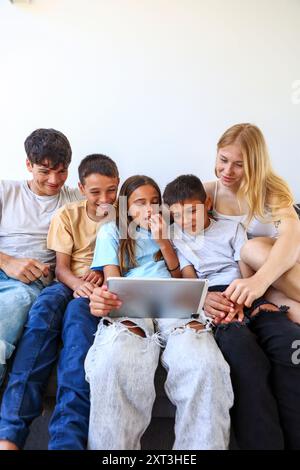 Trois frères et sœurs, qui sont des triplés, assis étroitement ensemble et partageant une tablette, le groupe montre des émotions diverses pendant qu'ils s'engagent avec le co numérique Banque D'Images