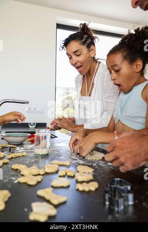 Un joyeux moment en famille capturé alors qu'une mère et un enfant s'engagent à préparer des biscuits ensemble dans un cadre de cuisine moderne, exprimant le plaisir et l'esprit d'équipe Banque D'Images