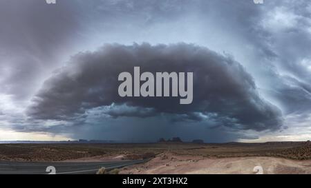 Une vue panoramique de Monument Valley tandis qu'un énorme nuage d'orage se profile au-dessus de vous, projetant des ombres spectaculaires sur les formations rocheuses rouges emblématiques et l'atmosphère stérile Banque D'Images