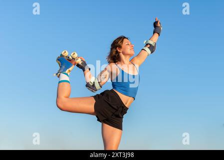 Une jeune femme exécute habilement un tour de patin à roulettes dans un skate Park, vêtue de vêtements de sport, mettant en valeur l'agilité et l'équilibre contre un bleu clair s. Banque D'Images