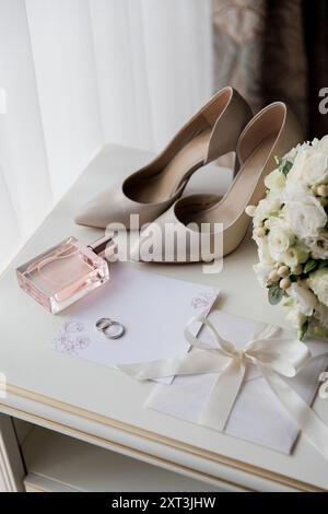 Essentiels de mariage de la mariée : talons, bouquet, bagues, parfum, et invitation sur une table blanche Banque D'Images