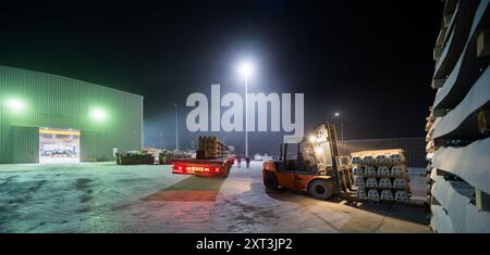 Cadre de nuit industriel avec chariot élévateur chargeant des traverses de chemin de fer sur un camion, mettant en évidence la logistique dans les éléments de design intérieur. Banque D'Images