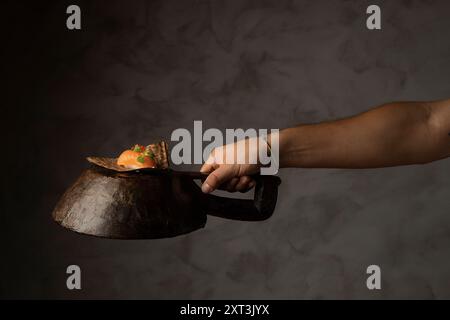 Une vue artistique d'une main arrangeant des sushis sur une poêle en fer rustique, soulignant l'élégance de la préparation des sushis dans un éclairage de humeur sombre Banque D'Images