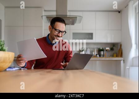 Conseiller financier masculin souriant tenant des rapports et travaillant sur ordinateur portable au bureau dans le bureau à domicile Banque D'Images