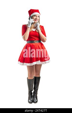 Jeune femme latine habillée comme le père noël souriant regardant la caméra parlant sur le téléphone portable sur fond blanc à noël Banque D'Images