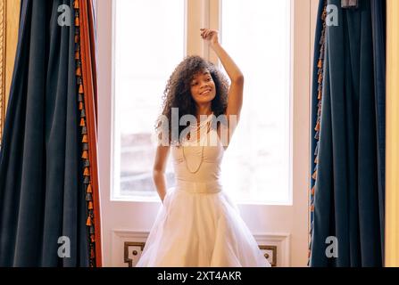 Charmante femme africaine aux cheveux bouclés dans une élégante robe blanche se tient près des portes rétro décorées et se tient sur le cadre. Jolie fille noire porte perle j Banque D'Images