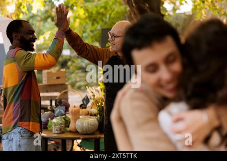 Image détaillée de vendeurs heureux accueillant des clients avec cinq hauts, appréciant le shopping le jour ensoleillé au stand du marché des agriculteurs. Des gens multiraciaux serrant la main, s'amusant au festival de la nourriture. Banque D'Images