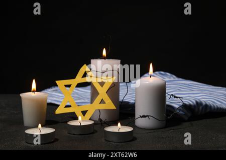 Uniforme de prisonnier, bougies allumées et étoile de David sur fond sombre. Journée internationale de commémoration de l'Holocauste Banque D'Images