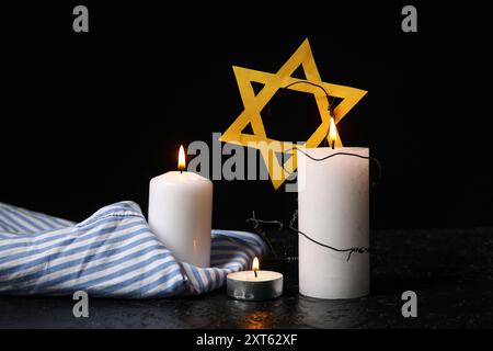 Uniforme de prisonnier, bougies allumées et étoile de David sur fond sombre. Jour du souvenir de l'Holocauste Banque D'Images