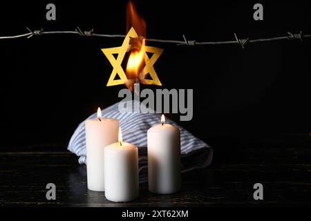 Uniforme de prisonnier, étoile brûlante de David, bougies incandescentes et fil de fer barbelé sur fond sombre. Jour du souvenir de l'Holocauste Banque D'Images