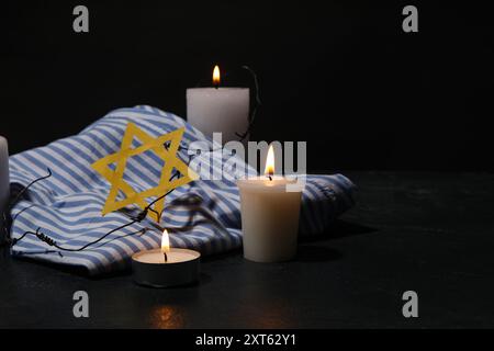 Uniforme de prisonnier, bougies allumées et étoile de David sur fond sombre. Jour du souvenir de l'Holocauste Banque D'Images