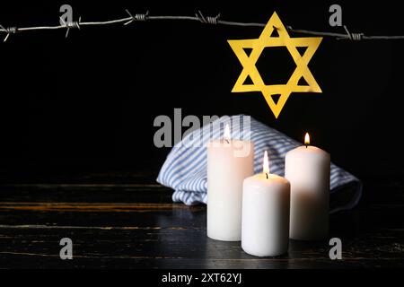 Uniforme de prisonnier, étoile de David, bougies allumées et barbelés sur fond sombre. Jour du souvenir de l'Holocauste Banque D'Images