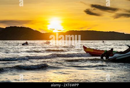 Langkawi Island, Malaisie-mai 01 2023 : le soleil se couche derrière les petites îles malaisiennes au-delà, et les jetskis jouent parmi les vagues tandis que les propriétaires apportent leurs bateaux Banque D'Images